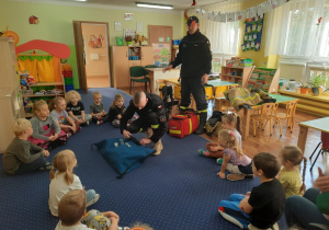 Dzieci siedzą na dywanie i słuchają o pracy strażaka.