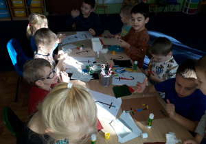 Dzieci siedzą przy stole i wykonują wydzierankę z kolorowego papieru.