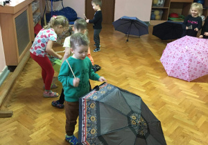 Dzieci na sali gimnastycznej bawią się z wykorzystaniem parasolek.