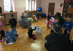 Dzieci na sali gimnastycznej bawią się z wykorzystaniem parasolek.