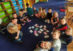 Dzieci siedzą w kole na dywanie, a przed nimi wycięte zaprojektowane wcześniej karty bankomatowe.