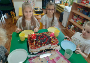 Dziewczynki siedzą przy stole przed nimi stoi tort.