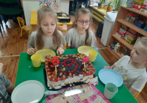 Dziewczynki siedzą przy stole i zdmuchują świeczki.