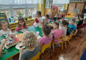Dzieci siedzą przy stole i zjadają słodkości przygotowane przez mamę dziewczynek.