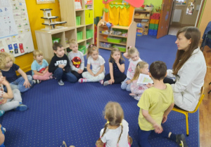 Dzieci siedzą w kole na dywanie i słuchają pani dietetyk.