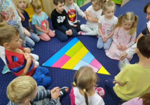 Dzieci siedzą w kole na dywanie, a przed nimi leży piramida zdrowego żywienia.