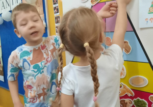 Dzieci uzupełniają piramidę zdrowego żywienia zamocowaną do tablicy.