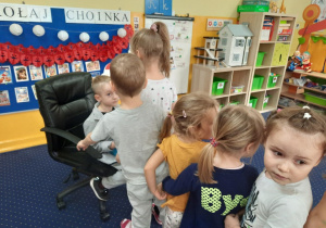 Chłopiec siedzi na krześle, a dzieci podchodzą i składają mu życzenia.