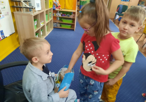Chłopiec siedzi na krześle, a dzieci podchodzą i składają mu życzenia.