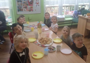 Dzieci siedzą przy stole na którym stoją słodkości.