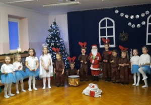 Dzieci ustawione w półkolu grają na instrumentach.