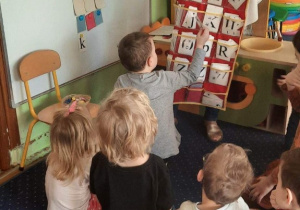 Dzieci siedzą na dywanie, chłopiec wyjmuje literkę.