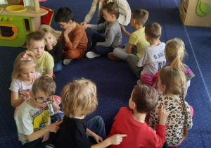Dzieci siedzą na dywanie w kole i piszą sobie na plecach.