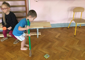 Chłopiec przesuwa kijkiem woreczek na sali gimnastycznej.