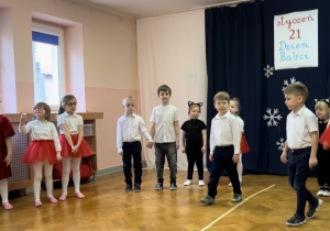 Dzieci ustawione w półkolu, dwóch chłopców wychodzi na środek sali.