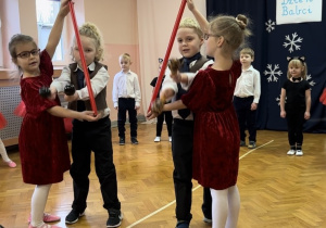 Dzieci ustawione w półkolu śpiewają piosenkę, czworo tańczy na środku sali.