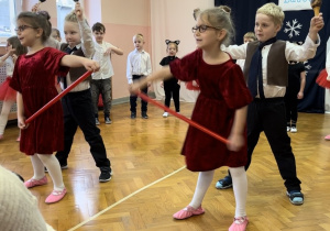 Dzieci ustawione w półkolu śpiewają piosenkę, czworo tańczy na środku sali.