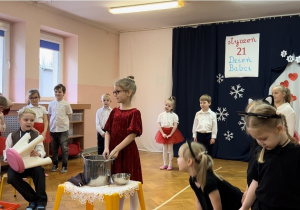 Dzieci ustawione w półkolu, na środku sali kilkoro dzieci odgrywa scenkę rodzajową "Codzienność u Gieni i Stefana".