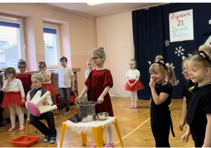 Dzieci ustawione w półkolu, na środku sali kilkoro dzieci odgrywa scenkę rodzajową "Codzienność u Gieni i Stefana".
