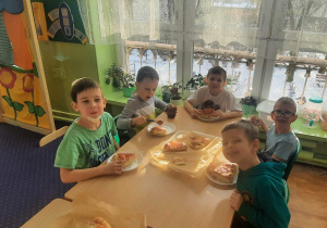 Dzieci siedzą przy stolikach i przygotowują pizzę.