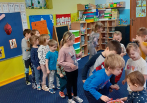 Dzieci ustawione w rządku podchodzą do chłopca składając mu życzenia i biorą cukierka.