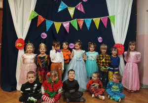 dzieci w przebraniach stoją na tle napisu "Karnawał", pozują do zdjęcia grupowego