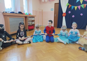 dzieci w przebraniach siedzą na podłodze, trzymają sigumę