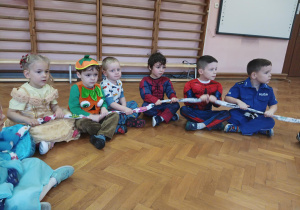 dzieci w przebraniach siedzą na podłodze, trzymają sigumę