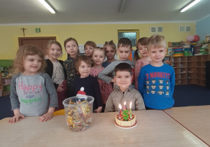 Dzieci zgromadzone wokół stołu pozują do zdjęcia. na stole stoi tort.