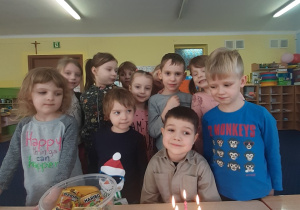 Dzieci zgromadzone wokół stołu pozują do zdjęcia. na stole stoi tort.