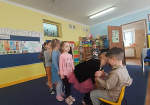 Chłopiec siedzi na krześle, pozostałe dzieci ustawione w rządku składają mu życzenia.