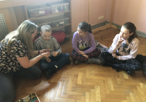 Dzieci siedzą na podłodze w kole i oglądają makarony.