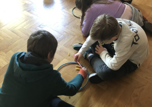 Dzieci siedzą na podłodze w parach i łowią słomką makaron.