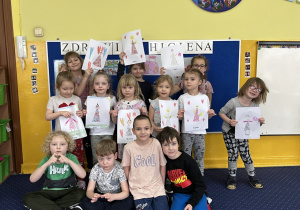 Wspólne zdjęcie wszystkich dzieci. Dziewczynki trzymają laurki wykonane przez chłopców.