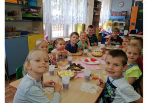 Dzieci przy stole jedzą słodycze.