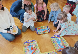 dzieci siedzą na podłodze sali gimnastycznej, rozwiązują zagadki