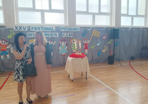 na sali gimnastycznej stoją dwie kobiety, obok nich na stoliku widać tort z świeczkamiie