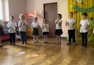 Dzieci stoją w półkolu i grają na instrumentach.