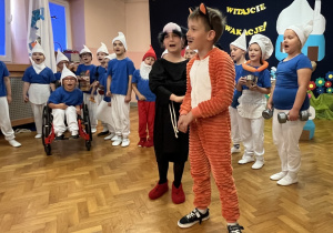 Smerfy stoją w półkolu, a przed nimi stoi Gargamel i Klakier.