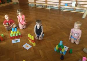 Dzieci siedzą na podłodze i bawią się kolorowymi kubeczkami.