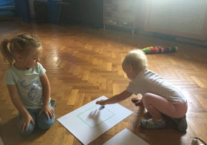 Dzieci siedzą na podłodze i obserwują jadącego ozobota.