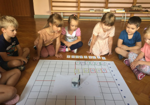 Dzieci siedzą na podłodze i obserwują rysującego genibota.
