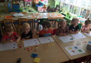 Dzieci siedzą przy stolikach i układają kompozycje z figur geometrycznych.