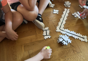 Dzieci siedzą na podłodze i układają drogę z puzzli dla ozobota.