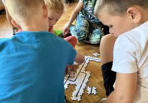 Dzieci siedzą na podłodze i układają drogę z puzzli dla ozobota.