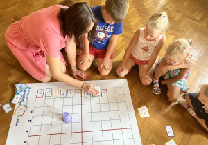 Dzieci siedzą na podłodze i obserwują kodowanie genibota.