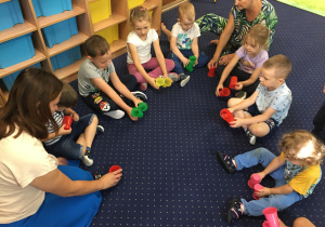 Dzieci siedzą na dywanie i bawią się kolorowymi kubeczkami.