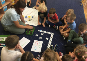 Dzieci siedzą na dywanie i obserwują programowanie ozobota z wykorzystaniem puzzli.
