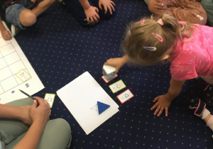 Dzieci siedzą na dywanie i programują genibota.