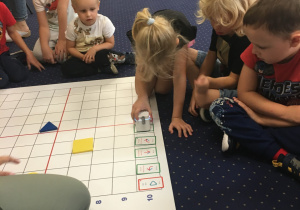 Dzieci siedzą na dywanie i programują genibota.